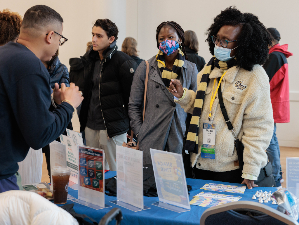 Parent and student talking with a GW staff member at a resource fair table
