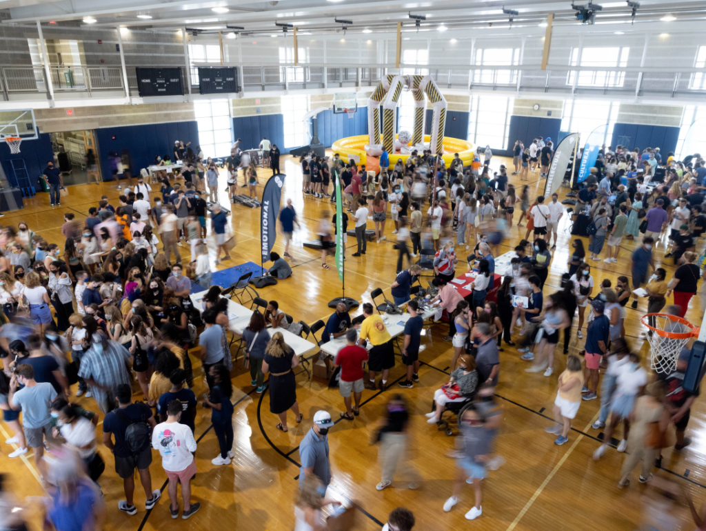 A large crowd of families and students mingles among tables of resources and campus partners at the Raise Up Community Fair during Orientation
