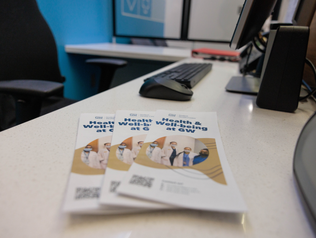 A stack of brochures on a desk, title reads "Health & Well-being at GW"